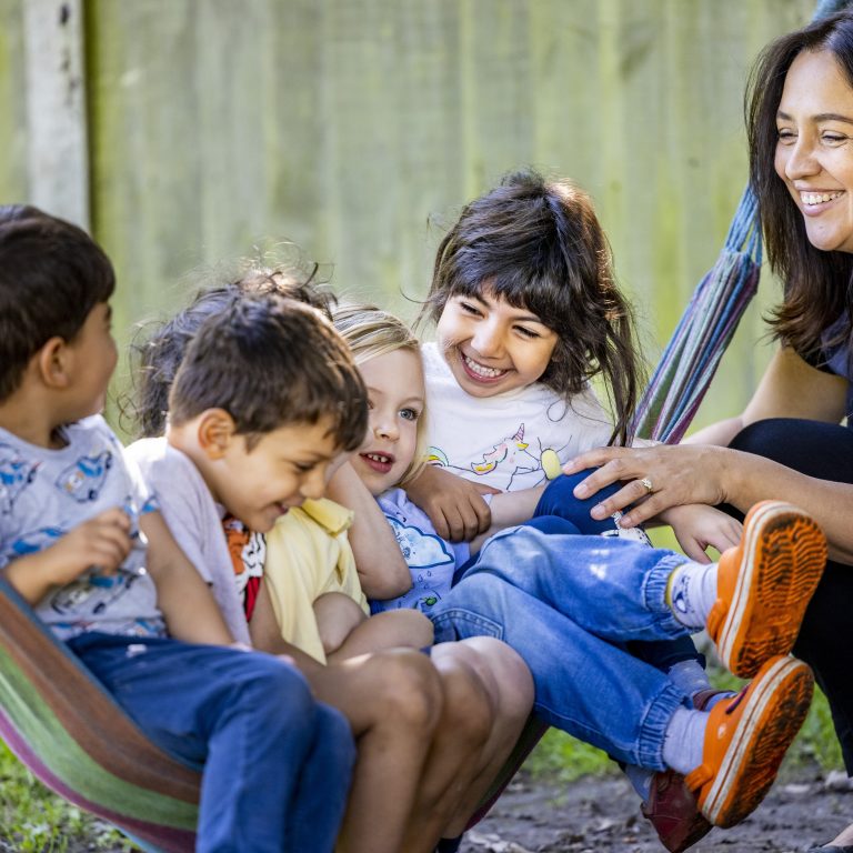 5 children in a hammock as a teacher looks on to provide support